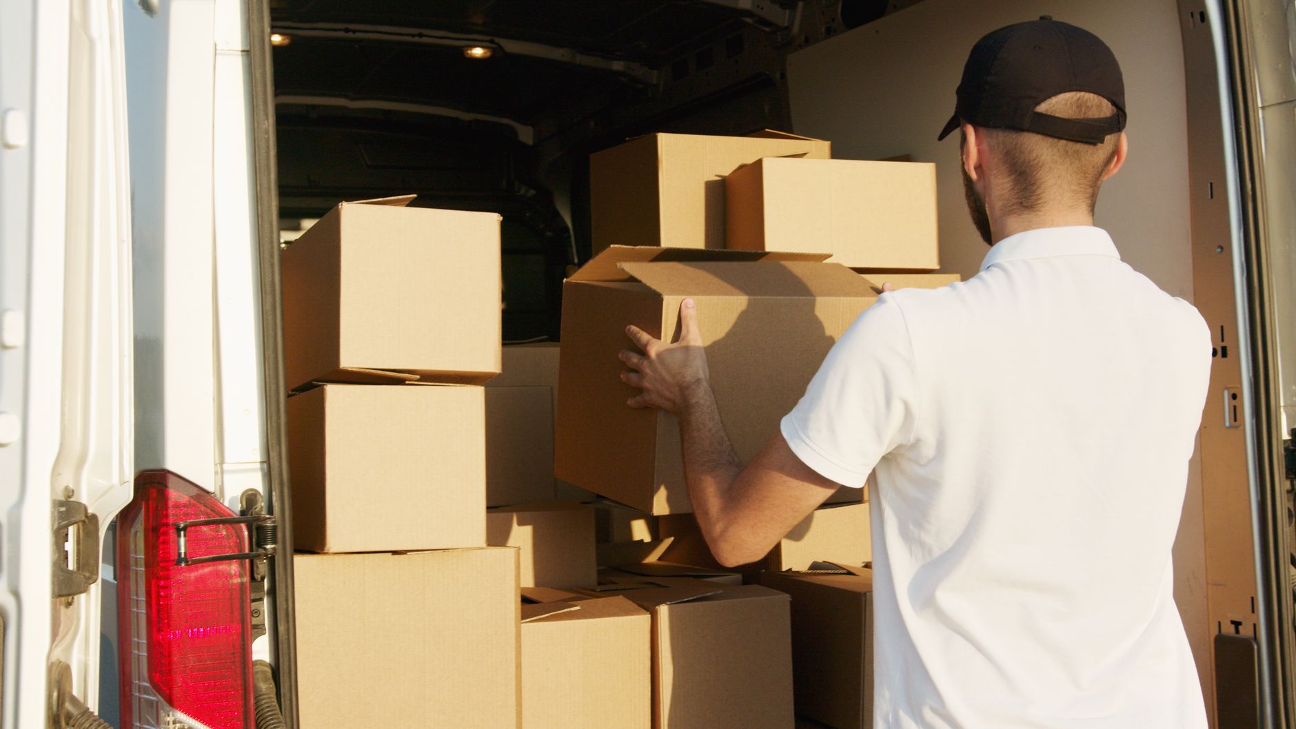 A driver loading cardboard boxes into the back of a white van