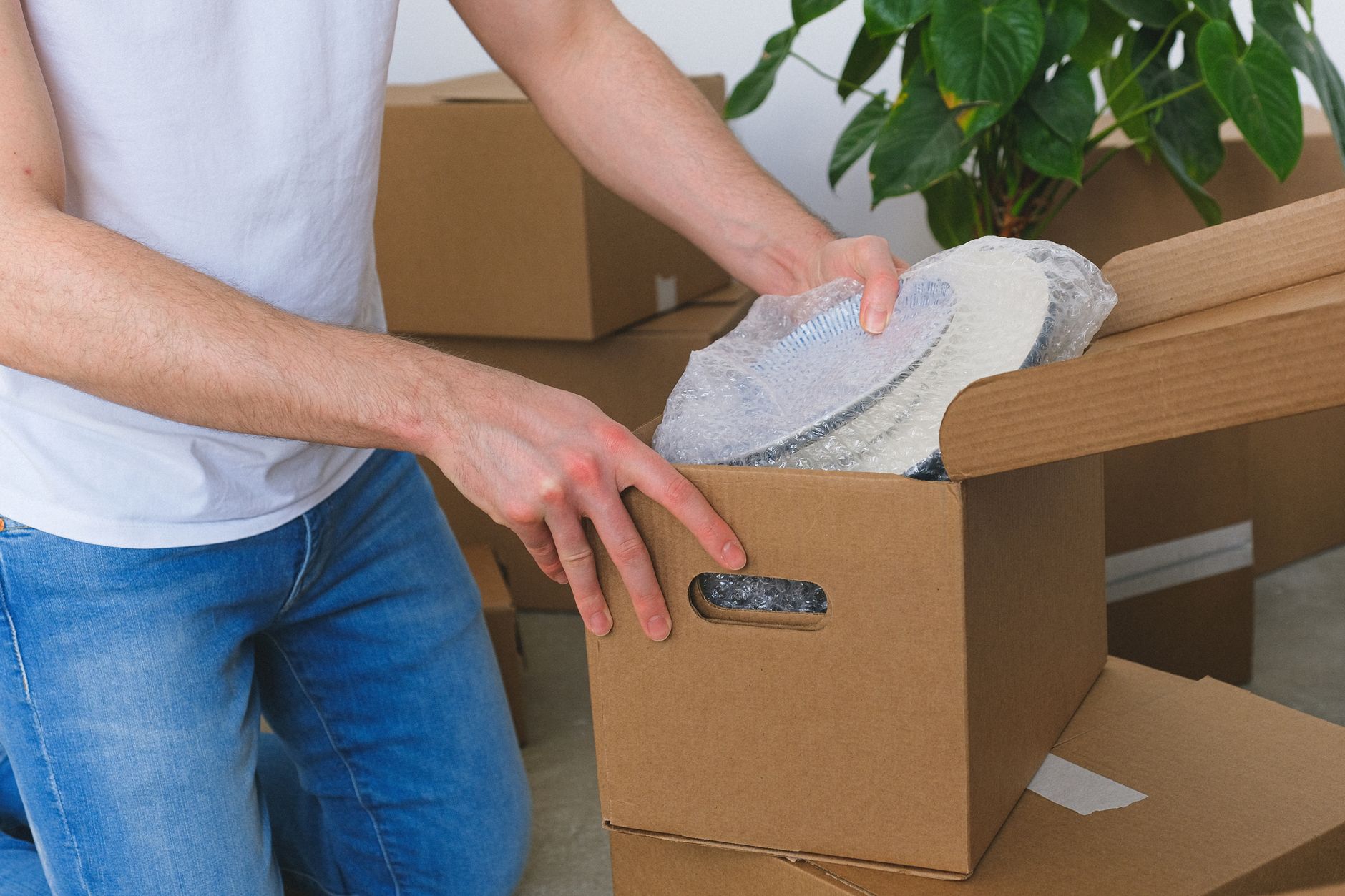 A person placing individually bubble-wrapped plates inside an open cardboard box