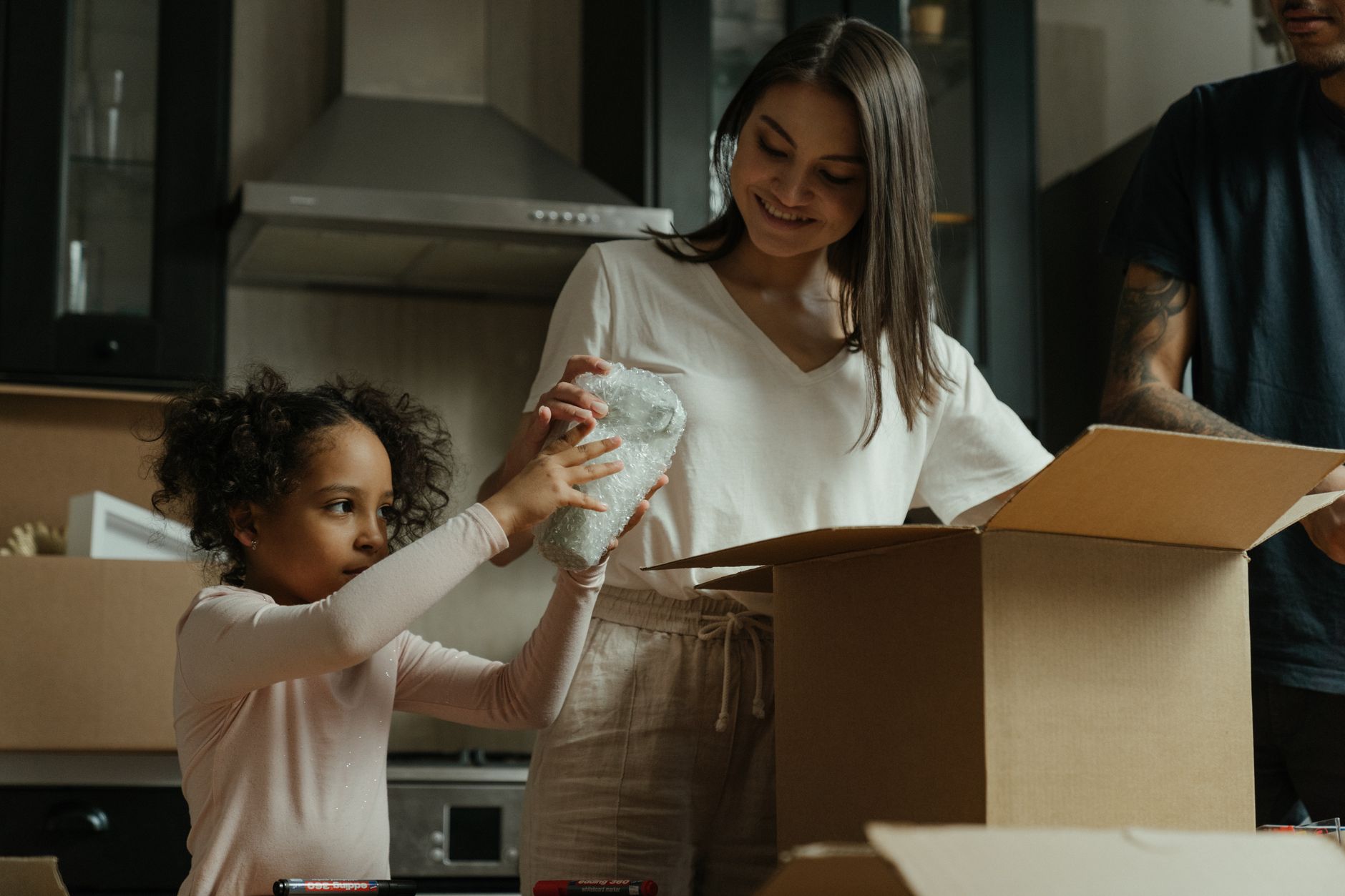 A parent and child unpacking a box together in a new kitchen