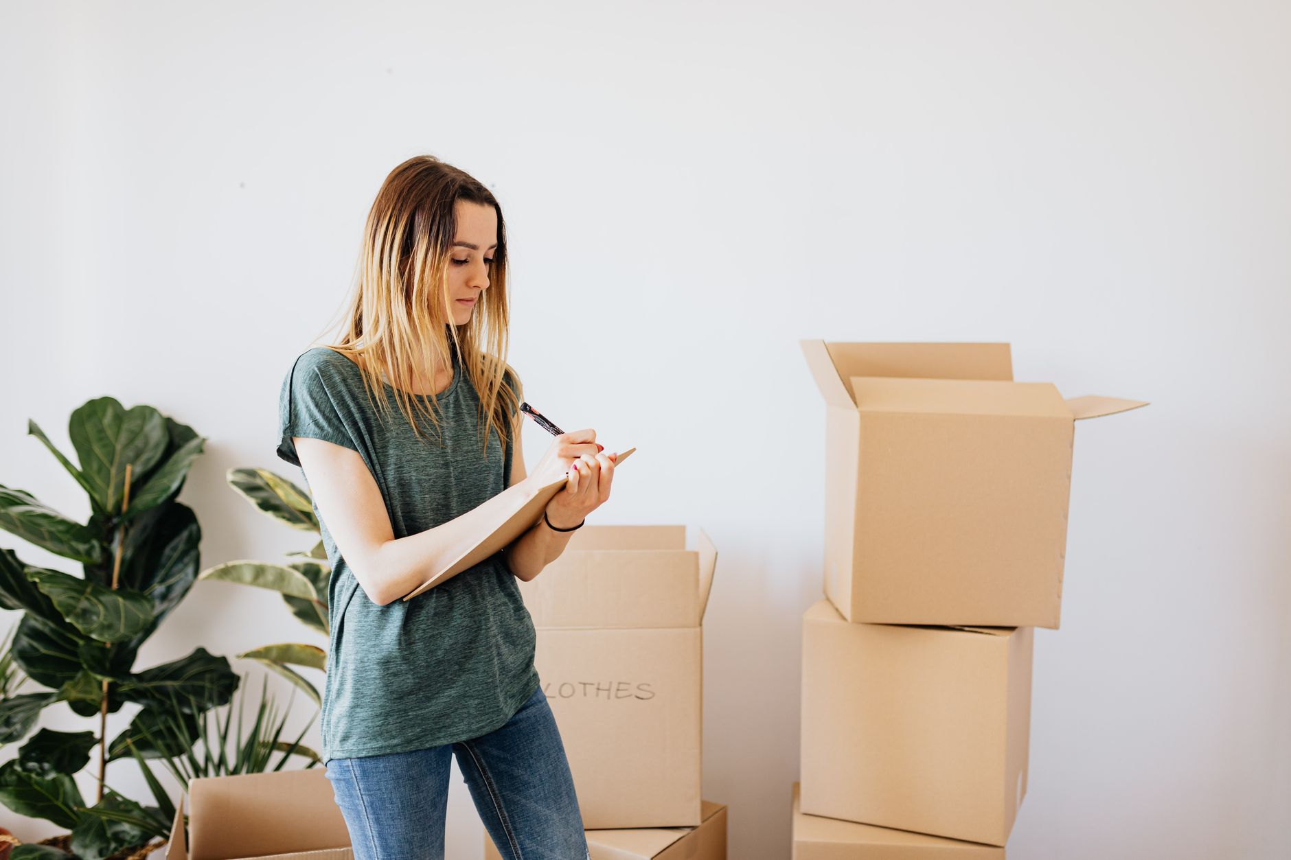 A woman writing a moving checklist beside stacked cardboard boxes