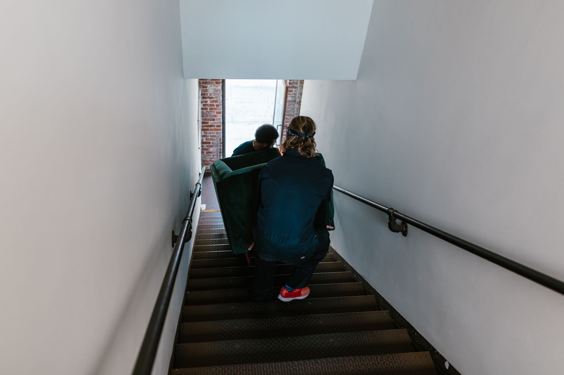 Two people carrying a sofa down a narrow staircase