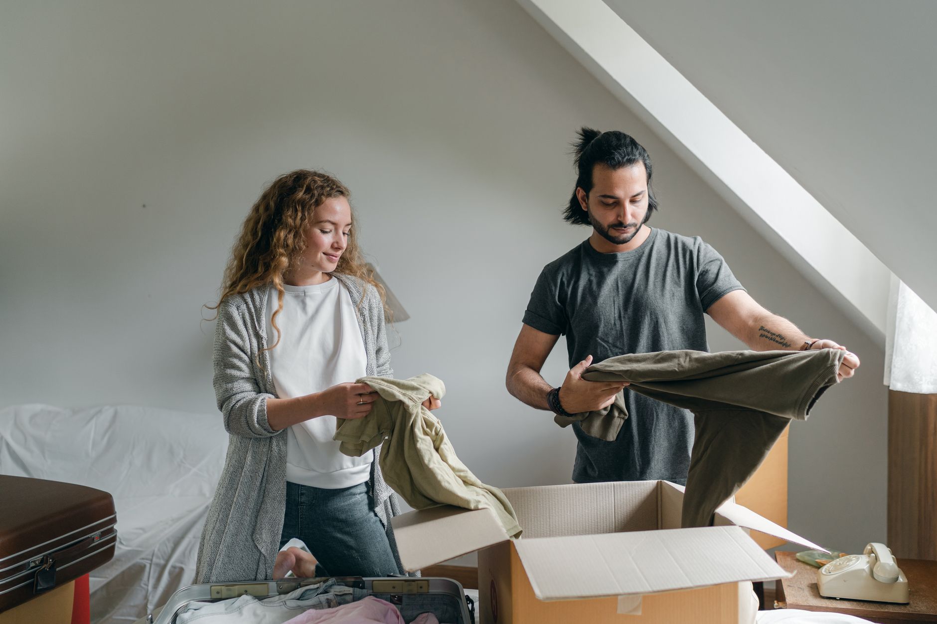 Two students packing clothes and boxes in a bedroom before moving