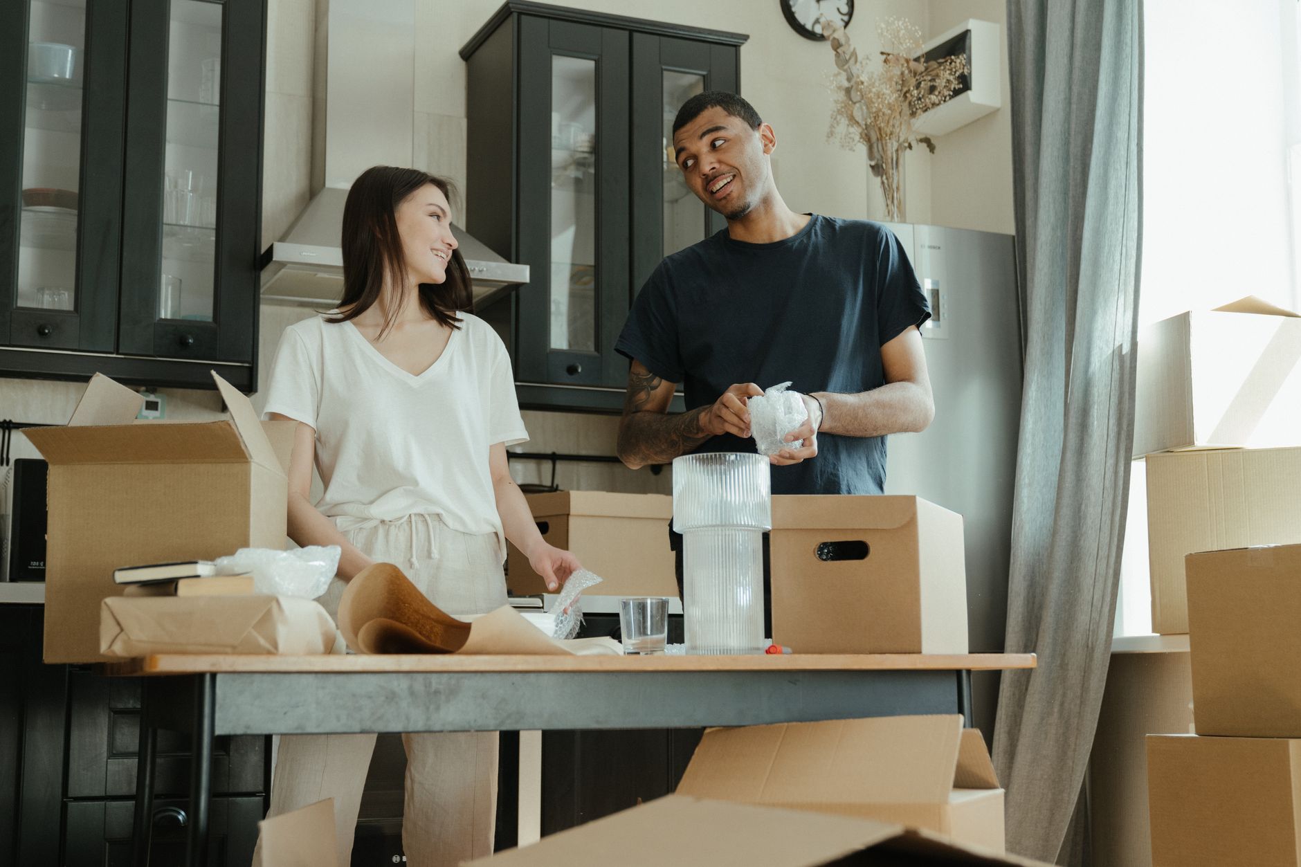 Two people wrapping kitchen items beside moving boxes