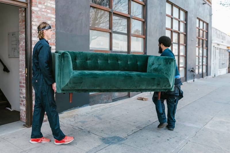 Two people carrying a sofa out to a van
