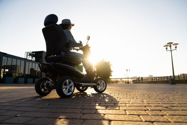 A person riding a mobility scooter along a promenade at sunset